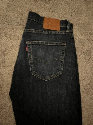 Levi's 502 mörkblå jeans W34 L34 - Snygga Levi's 502 jeans i mörkblå tvätt med klassiska fem fickor och bruna sömmar. Modellen har rak passform och normal midja, tillverkade i slitstarkt jeanstyg. Perfekt för dig som gillar en tidlös look med lite smalare ben.