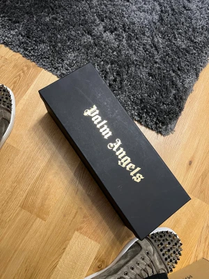 Palm Angels svarta sandaler - Svarta slides från Palm Angels med vit logotyp i gotisk stil över foten. Snygg och clean design med platt sula och rund tå. Tillverkade i syntetmaterial som är både slitstarkt och bekvämt. Kommer med originalkartong.