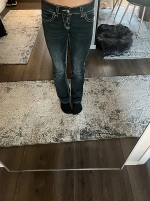 Mörkblå jeans med broderade bakfickor - Snygga mörkblå jeans med kontrastsömmar och broderade detaljer på bakfickorna. Modellen har låg midja och raka ben med lätt bootcut. Jeansen har klassisk femficksdesign och är tillverkade i denim med stretch för skön passform.