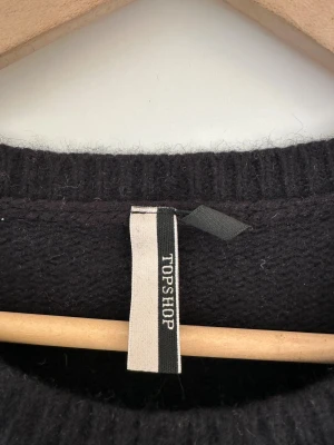 Svart stickad tröja från Topshop - Härlig svart stickad tröja i ull och angora-blandning från Topshop. Långa ärmar och en rund halsringning. Elegant och håller värmen bra. Storlek 38-40.   Hämtas i Stockholm eller skickas mot porto