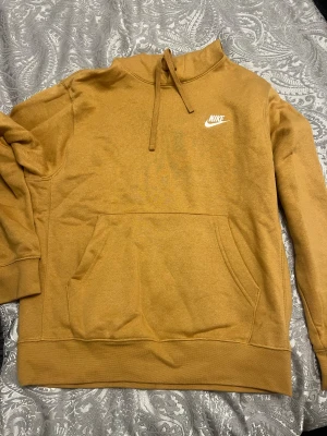 Nike hoodie - Säljer en brun/gul  hoodie från Nike med vit logga på bröstet. Tröjan har snörning i halsen, stor magficka och långa ärmar. Perfekt för chill dagar och har en skön, mjuk känsla tack vare bomullsmaterialet.