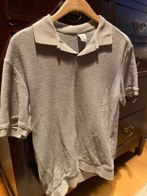 Grå pikétröja från Zara - Snygg grå pikétröja från Zara i storlek S. Tröjan har klassisk krage, korta ärmar och är tillverkad i ett strukturerat, stickat material som ger en cool vibe. Perfekt för dig som gillar stilrena och enkla plagg med lite edge.