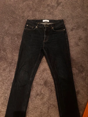 Svarta jeansbyxor från Whyred - Säljer ett par mörkblå jeansbyxor från Whyred med klassisk femficksdesign och raka ben. Jeansen har mörk tvätt, kontrastsömmar och normal passform. Perfekta för dig som gillar stilrena och enkla jeans i bomull.