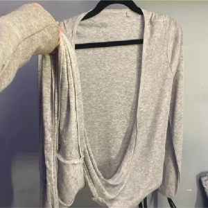 Grå omlottkofta med knytband - Mjuk och tunn grå kofta i omlottmodell med långa ärmar och knytband framtill. Perfekt att slänga över en topp för en chill look. Enkel design utan mönster och i en ljusgrå nyans.