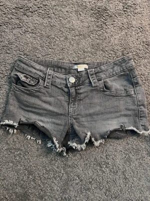 Grå jeansshorts med fransig kant Gina Tricot - Snygga grå jeansshorts från Gina Tricot i storlek 152. Modellen har låg midja, klassiska fem fickor och fransig, rå kant nedtill för en cool vibe. Perfekt för dig som gillar en avslappnad och trendig stil. Materialet är bomull och passformen är normal.