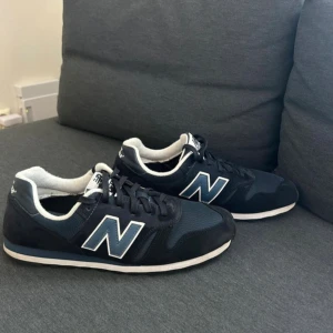 Mörkblå New Balance sneakers 373 storlek 44 - Snygga mörkblå sneakers från New Balance med vit kant och stor N-logga på sidan. Skorna har snörning, platt sula och rund tå. Ovandelen är i mesh och mocka för en sportig vibe. Perfekta för dig som gillar klassisk streetstil och vill ha bekväma skor till vardags nypris 1099kr.
