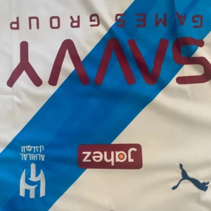 Vit Neymar Jr. fotbollströja Puma - Snygg vit fotbollströja med blå diagonal rand, Neymar Jr. och nummer 10 på ryggen. Puma-logga på bröstet och flera tryckta sponsorer. Klassisk passform med korta ärmar och rund hals. Perfekt för dig som älskar fotboll och vill sticka ut på planen.