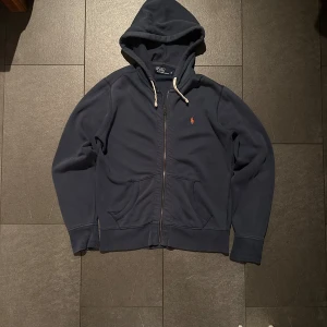 Zip tröja från Ralph Lauren - Blå (Herr M) - Snygg mörkblå Zip från Ralph Lauren. Tröjan är i gott skick men har två fläckar (se bilder) som kanske går bort i tvätt. Det syns dock knappast. Nypris ligger runt ca 2200kr
