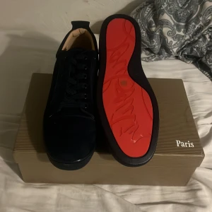  mörkblå sneakers - Snygga mörkblå sneakers med klassisk röd sula och broderad logga på hälen. Skorna har rund tå, platt sula och är tillverkade i mocka med svarta snören. Kommer med originalpåse och äkthetsbevis från Paris.