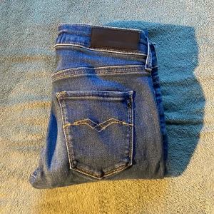 Blå Replay jeans, storlek 29/32 - Säljer ett par klassiska blå jeans från Replay med snygga kontrastsömmar på bakfickan och läderpatch i midjan. Jeansen har rak passform och är tillverkade i slitstarkt denimtyg. Perfekta för dig som gillar stilrena och tidlösa jeans.