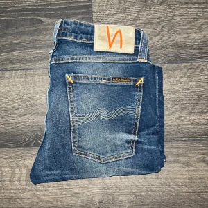 Nudie Jeans  - Säljer ett par blå skinny jeans från Nudie Jeans med klassisk orange söm och vågig brodyr på bakfickorna. Jeansen har hög midja och är tillverkade i stretchig bomull för en tight passform. Snyggt slitna detaljer framtill och bak. Modell skinny Lin. Midjemått 35cm, längd 96cm. Ifall det inte finns någon bild i annonsen där jag bär plaggen jag säljer så är det för att jag ej kan ha storleken heller passformen, så kolla måtten för storlek och googla på modellnamnet för passform 😉s2