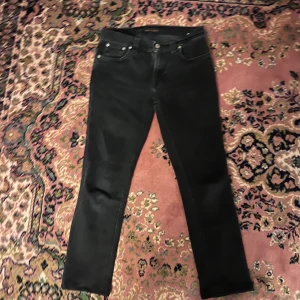 Svarta slim jeans från Nudie Jeans 28/30 - Svarta skinny jeans från Nudie Jeans med klassisk femficksdesign och tydliga sömmar på bakfickorna. Jeansen har en smal passform och är tillverkade i stretchig denim för extra komfort. Snyggt läderpatch med Nudie-logga baktill i midjan. Midja 36cm längd 86cm (56)
