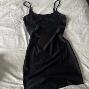 Svart kort klänning med smala axelband - Säljer en svart kort klänning med smala axelband och enkel design. Klänningen har en figurnära passform och är perfekt för dig som gillar minimalistisk stil. Materialet känns mjukt och följsamt mot huden.