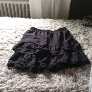 Svart volangkjol från Gina Tricot - Svart kortkjol från Gina Tricot med två lager volanger och spetsdetaljer längs kanterna. Pris kan diskuteras