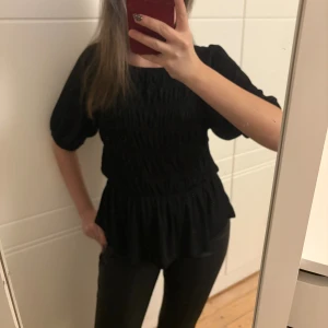 Svart smockad topp - Säljer denna supersnygga smockade toppen från Lindex i jättebra skick! Perfekt både till vardags och till speciella tillfällen!