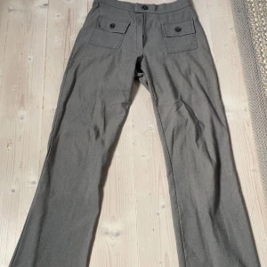 Gråa vida kostymbyxor med fickor - Snygga vintage grå kostymbyxor med vida ben och två stora fickor framtill med knappar. Materialet känns mjukt och har en lätt struktur.