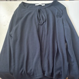 Svart långärmad tröja med knyt - Svart långärmad tröja från 157 med rund halsringning och snygg knytning framtill. Tröjan är i mjuk bomull och har en enkel, stilren design som passar perfekt till jeans eller kjol.