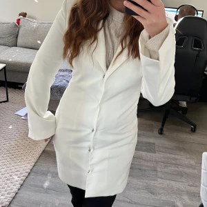 Vit lång kavaj med knappar från Nelly - Snygg vit lång kavaj med klassisk krage och raka linjer. Kavajen har knäppning framtill med flera knappar och är tillverkad i ett slätt. Silkes på insidan