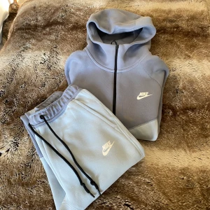 Nike Tech Fleece hoodie ljusblå/vit logga  - Nike Tech Fleece hoodie/byxa i ljusblå  med vit logga, med hel dragkedja, huva och svarta detaljer. Jackan har två fickor med dragkedja och klassisk Nike-logga på bröstet. Perfekt för en sportig och chill stil. Finns inga defekter och är hel. 
