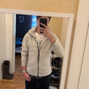 Cardigan från C.P. Company - Säljer en clean vit/beige puffer cardigan från C.P. Company, modell Goggle Jacket med C.P. Shell soft shell stretch-tyg. Jackan har huva, svarta dragkedjor och quiltad design. Bra skick, som på bilderna  Storlek S, 44 Sällsynt, svår att hitta!