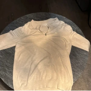 Beige half zip tröja från Lindbergh - Snygg beige långärmad tröja från Lindbergh med slim fit passform. Tröjan har en klassisk krage och half zip-dragkedja framtill samt diskret broderad logga på bröstet. Perfekt för dig som gillar stilrena och enkla plagg.