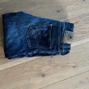 Mörkblå Replay jeansbyxor - Snygga mörkblå jeans från Replay med klassisk femficksdesign och tydliga kontrastsömmar på bakfickan. Byxorna har dragkedjegylf och är tillverkade i bomull med en liten del elastan för extra komfort. Perfekta för dig som gillar stilrena jeans med en cool touch.