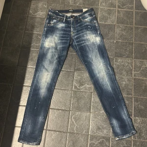 Jack & Jones Slim Glenn jeans blå 31/34 - Snygga blå jeans från Jack & Jones, modell Slim Glenn. Jeansen har en slim passform, klassisk femficksdesign och coola slitningar samt färgstänk för en trendig look. Tillverkade i bomull med gul kontrastsöm och medelblå tvätt. Jeansen är är gjorda i Italien!