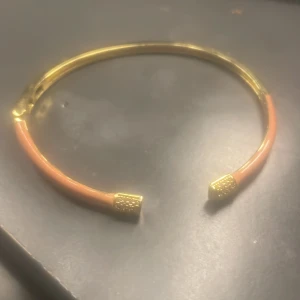 Guldigt armband med persikofärg - Snyggt armband i guldton med persikofärgad detalj och dekorativa guldiga ändar. Rostfri stål 