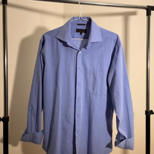 Blå skjorta med klassisk krage - Snygg blå skjorta från The Seven Seas med klassisk krage och bröstficka. Skjortan har långa ärmar och knäppning framtill. Perfekt för en stilren look och passar till många olika outfits.