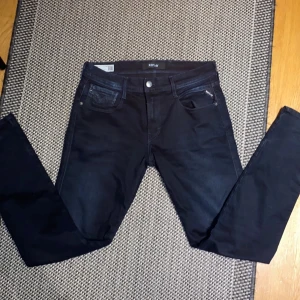 Svarta Replay Anbass slim jeans - Säljer ett par svarta Replay Anbass jeans i slim fit. Klassisk femficksmodell med snygga detaljer och diskret logga på bakfickan. Jeansen är tillverkade i stretchigt material för extra komfort och har en smal passform som sitter snyggt längs benen. Det är st 30x32.