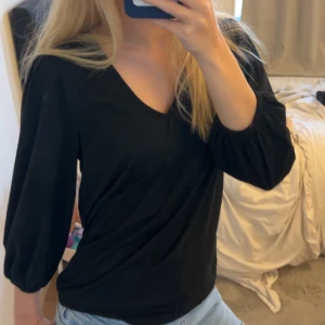 Svart v-ringad blus från KappAhl - Svart blus från KappAhl i storlek S. Modellen har v-ringning och trekvartsärmar med lätt puff och resår vid ärmslut. Toppens passform är normal och tyget känns mjukt och skönt mot huden. Perfekt till jeans eller kjol för en clean look.