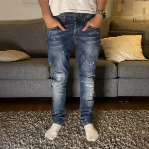 Dondup jeans  - Säljer ett par blå jeans från Dondup med slitningar och trasiga detaljer på knäna. Jeansen har en smal passform och klassiska fem fickor. Snygg tvätt med ljusare partier och coola slitningar för en trendig look.