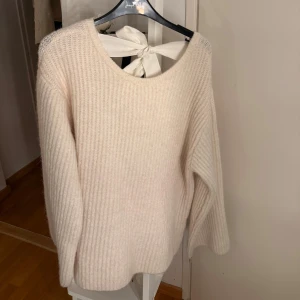 Stickad cremevit tröja med rosetta ryggen - Superfin stickad cremevit tröja från Gina Tricot med bred rosett i ryggen och öppen rygg. Tröjan har ribbad struktur, lång ärm och en mysig, lite fluffig känsla. Den är oversized!