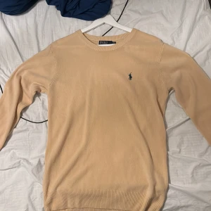 Beige stickad tröja Polo Ralph Lauren - Knappt använd snygg beige stickad tröja från Polo Ralph Lauren med klassisk rund hals och broderad grön logga på bröstet. Tröjan är i bomull och har ribbade muddar vid ärmslut och nederkant. Perfekt för en clean och stilren look. Är i storlek L.