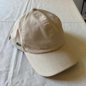 Lacoste keps i beige - En Lacoste keps i beige som är i mycket bra skick.