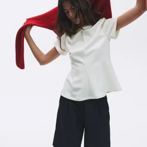 Vit kortärmad blus med enkel design - Säljer en stilren vit blus med korta ärmar och rund hals. Toppen har en lätt utsvängd passform och en diskret söm framtill som ger en snygg detalj. Perfekt att matcha med både jeans och kjol för en clean look.