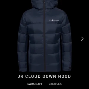 Mörkblå Sail Racing dunjacka med huva - Säljer en mörkblå dunjacka från Sail Racing med huva och dragkedja. Jackan är vadderad med 90% dun och 10% fjäder, yttertyg och foder i nylon. Snygg logga på bröstet och klassisk pufferstil som håller dig varm under kalla dagar. Hyfsat bra skick nått litet hål kring huvan men syns knappt! Jättesnygg 