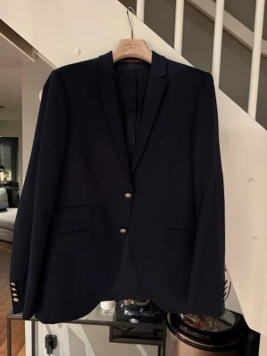 Mörkblå kavaj från Morris  - Stilren mörkblå kavaj med två knappar framtill och klassisk krage. Kavajen har tre fickor fram och dekorativa knappar vid ärmsluten. Perfekt för en dressad look och passar till många olika outfits. Morris 