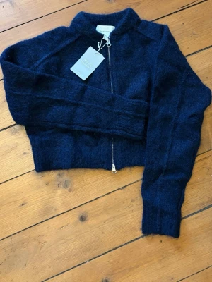 Mörkblå cardiganjacka från Andiata - Mysig mörkblå cardiganjacka från Andiata i fluffig ullblandning. Jackan har dragkedja framtill, ribbade muddar och en kort, boxig passform. Perfekt för lager-på-lager och en cool vardagslook.