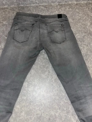 Grå Replay jeans med raka ben - Snygga grå jeans från Replay med klassisk femficksdesign och raka ben. Jeansen har diskreta slitningar och svarta detaljer vid fickorna. Perfekta för dig som gillar en stilren look med lite edge.
