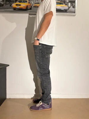 Mörkgrå jeans med slim fit - Snygga mörkgrå jeans med lätt tvättad look och klassiska fem fickor. Jeansen har en slim passform och raka ben, perfekt för en clean och modern stil. Tillverkade i mjukt bomullstyg med lite stretch för extra komfort.