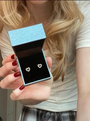Guldiga hjärtformade örhängen med blå stenar - Säljer ett par söta örhängen (studs) i form av små hjärtan. De är av guldbelagt sterling silver. De har små ljusblåa kristaller längs hela vägen. De är från Pico och ger ett klassiskt och gulligt intryck.