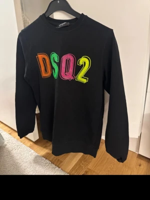 Hoodie  Dsquared2 - Svart sweatshirt från Dsquared2 med färgglad DSQ2-logga framtill. Klassisk modell med rund hals och bekväm passform. Original, med etikett och QR-kod kvar (se bild).