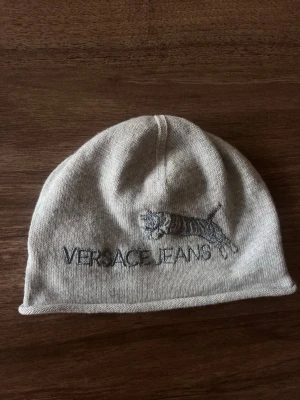 Mössa från Versace - Snygg grå mössa från Versace med broderad tiger och logga framtill. Mjukt material. 
