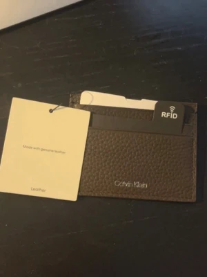 Brun Läderplånbok Calvin Klein - Slimmad brun kortplånbok från Calvin Klein i äkta läder med RFID-skydd. Plånboken har flera kortfack och stilren design med diskret logga framtill. Perfekt för dig som vill ha koll på korten utan att ta plats i fickan. Kommer med alla lappar samt orginal box (Helt ny aldrig använd)
