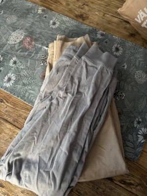 Två par mjukisbyxor i beige och grå - Från 12 år. Säljer två par mjukisbyxor, ett par i ljusbeige och ett par i ljusgrått. Båda har resår i midjan och vid bensluten för en skön och avslappnad passform. Perfekta för chill dagar hemma eller när du vill vara bekväm.
