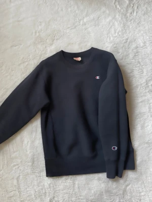 Svart sweatshirt från Champion - Klassisk grå sweatshirt från Champion med rund halsringning och logga broderad på bröstet och ärmen. 