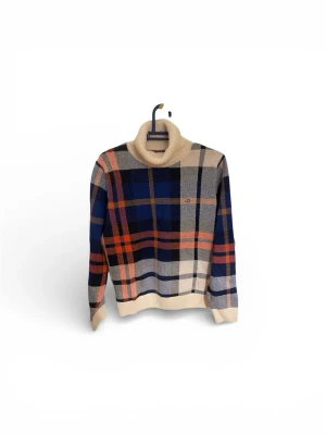 Rutig polotröja från Gant - Stickad polotröja från Gant med rutigt mönster i blått, beige, rött och orange. Tröjan har hög krage och ribbstickade muddar. Perfekt för dig som gillar klassisk och färgstark stil.