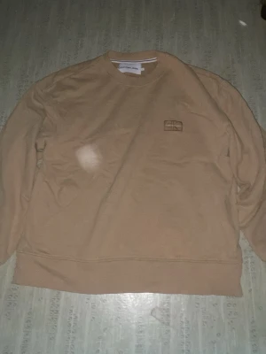 Beige sweatshirt från Calvin Klein Jeans - Snygg beige sweatshirt från Calvin Klein Jeans med broderad CK-logga på bröstet. Tröjan har rund halsringning, långa ärmar och ribbade muddar. Perfekt för en stilren och avslappnad look.