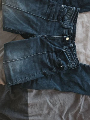 Mörkblå raka jeans med slitningar - Snygga mörkblå jeans med raka ben och diskreta slitningar framtill. Klassisk femficksmodell med silverfärgad knapp och dragkedja. Jeansen har en tvättad look och är tillverkade i denim, perfekt för en avslappnad stil.